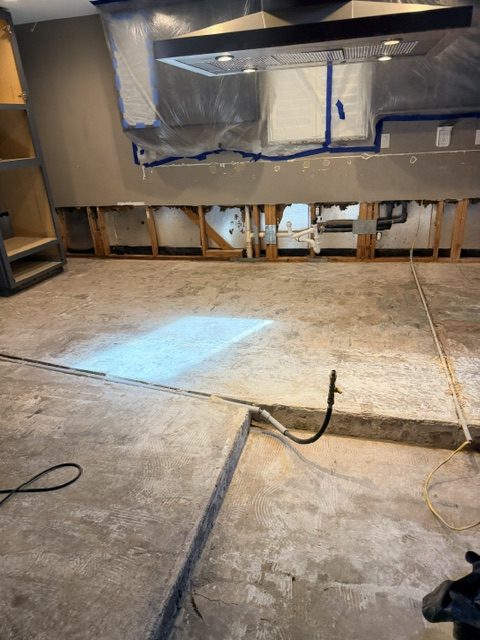 Kitchen flood cleanup with cut drywall, plastic containment around vent hood, and exposed studs ready for drying