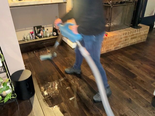 Flood Titan technician extracting water from damaged hardwood floor with professional extraction wand